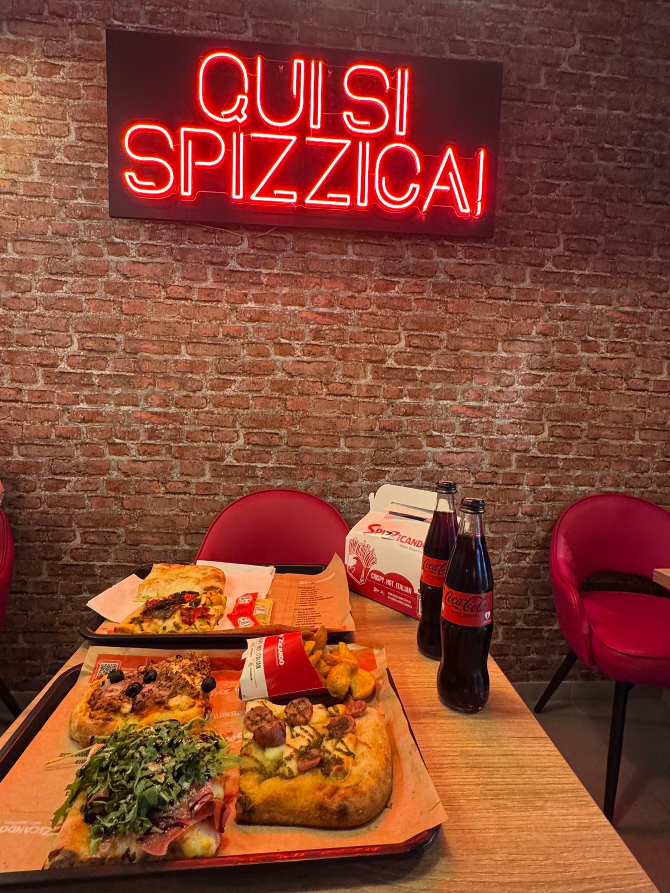Spizza al Taglio und Panino unter dem Neonschild „Qui si spizzica!“